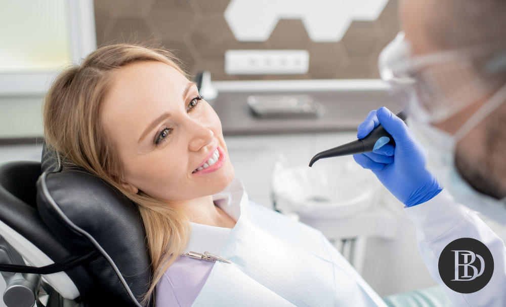 A young female patient smiles at their dentist who sits ready to begin treatment.