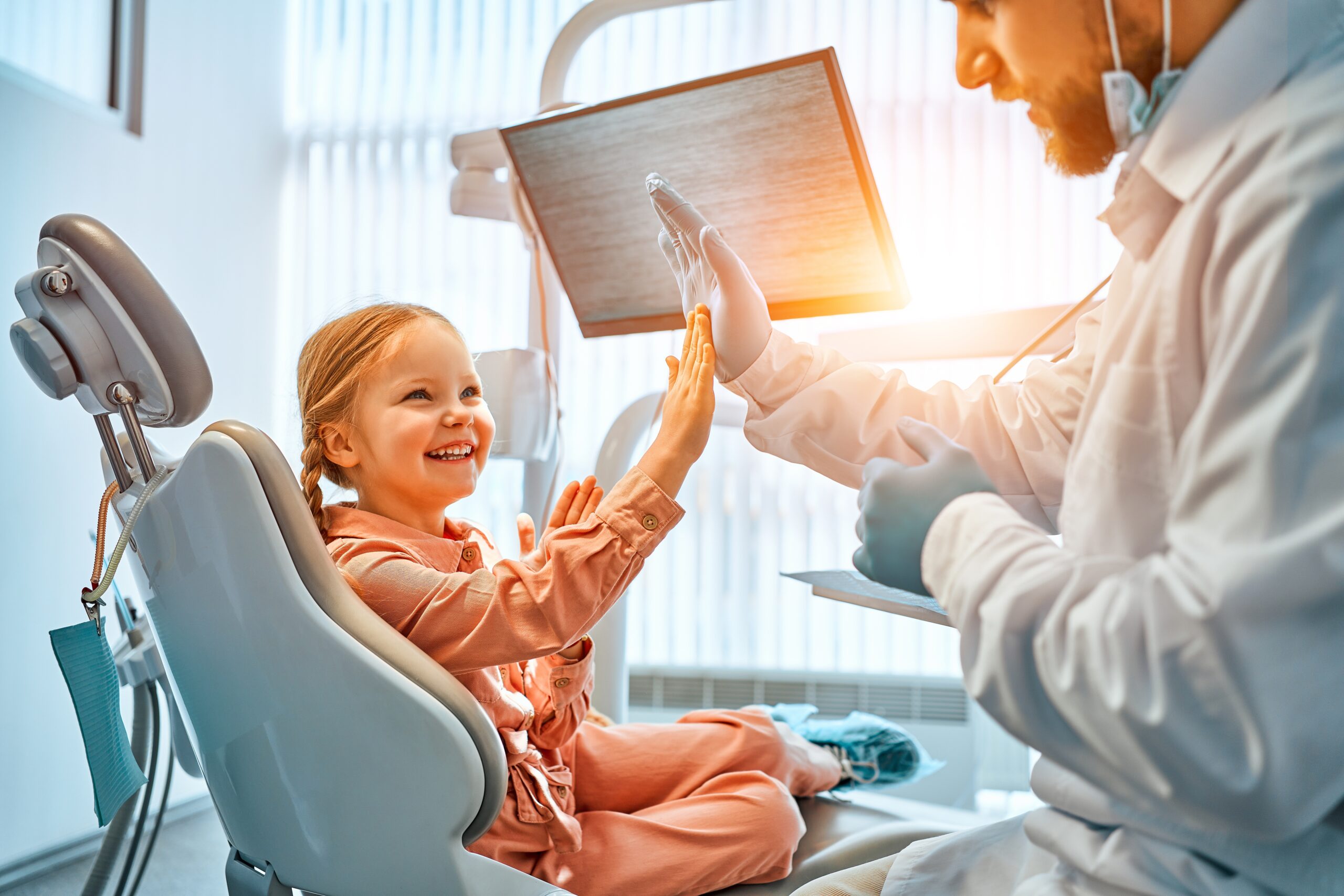 a little girl sitting in the dentist chair, high fiving the dentist